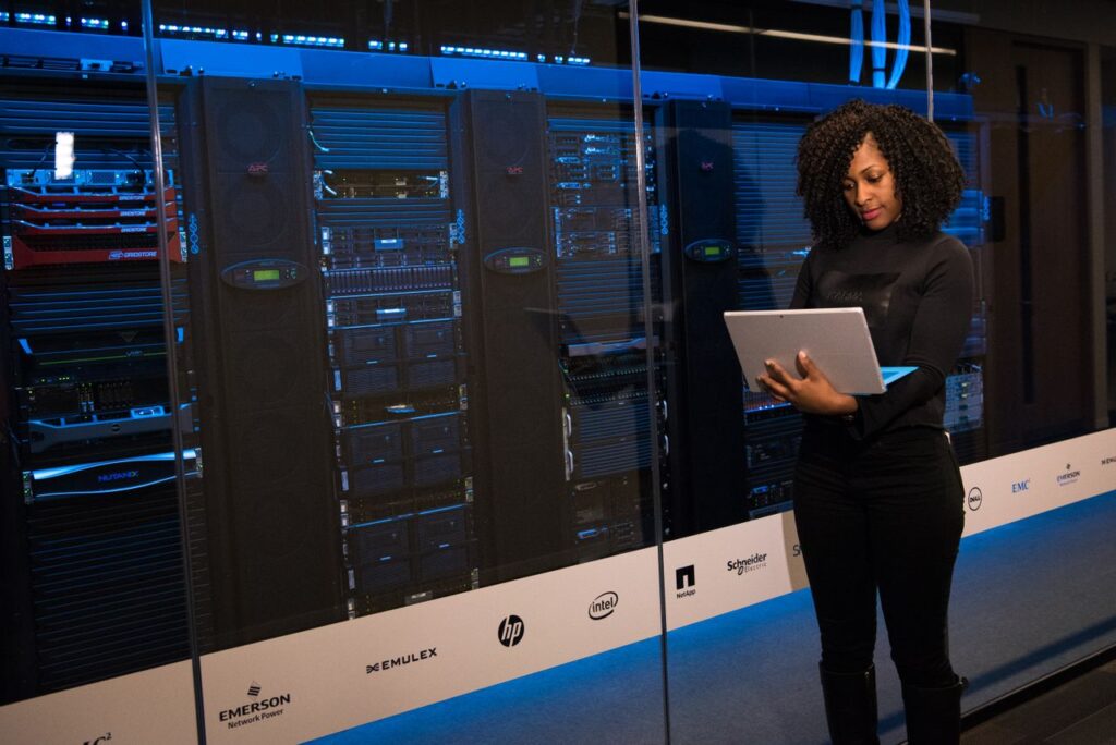 pexels photo 1181354 A female engineer using a laptop while monitoring data servers in a modern server room.